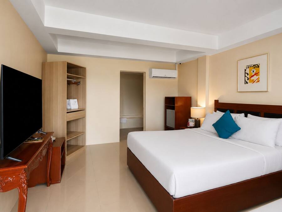 Une chambre d’hôtel avec un lit, une télévision, une commode en bois, une armoire et un tableau au mur.