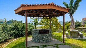 A gazebo with a stone fire pit, surrounded by a well-maintained garden with palm trees and a view of the sea. - Whiterock Beach Resort (Subic)