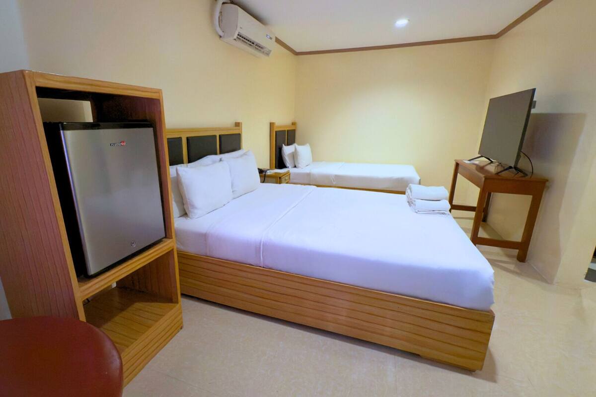 A hotel room with a bed, a TV, a refrigerator, and a TV stand.
