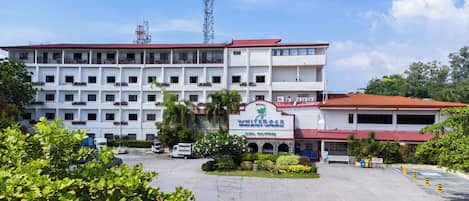 A multi-story hotel with a red roof and a sign indicating it is a beach hotel. There are several vehicles parked in front, and the area is surrounded by greenery.