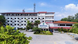 Un hôtel à plusieurs étages, avec un toit rouge et une enseigne indiquant qu’il s’agit d’un hôtel de plage. Plusieurs véhicules sont stationnés devant, et les environs sont bordés de verdure.