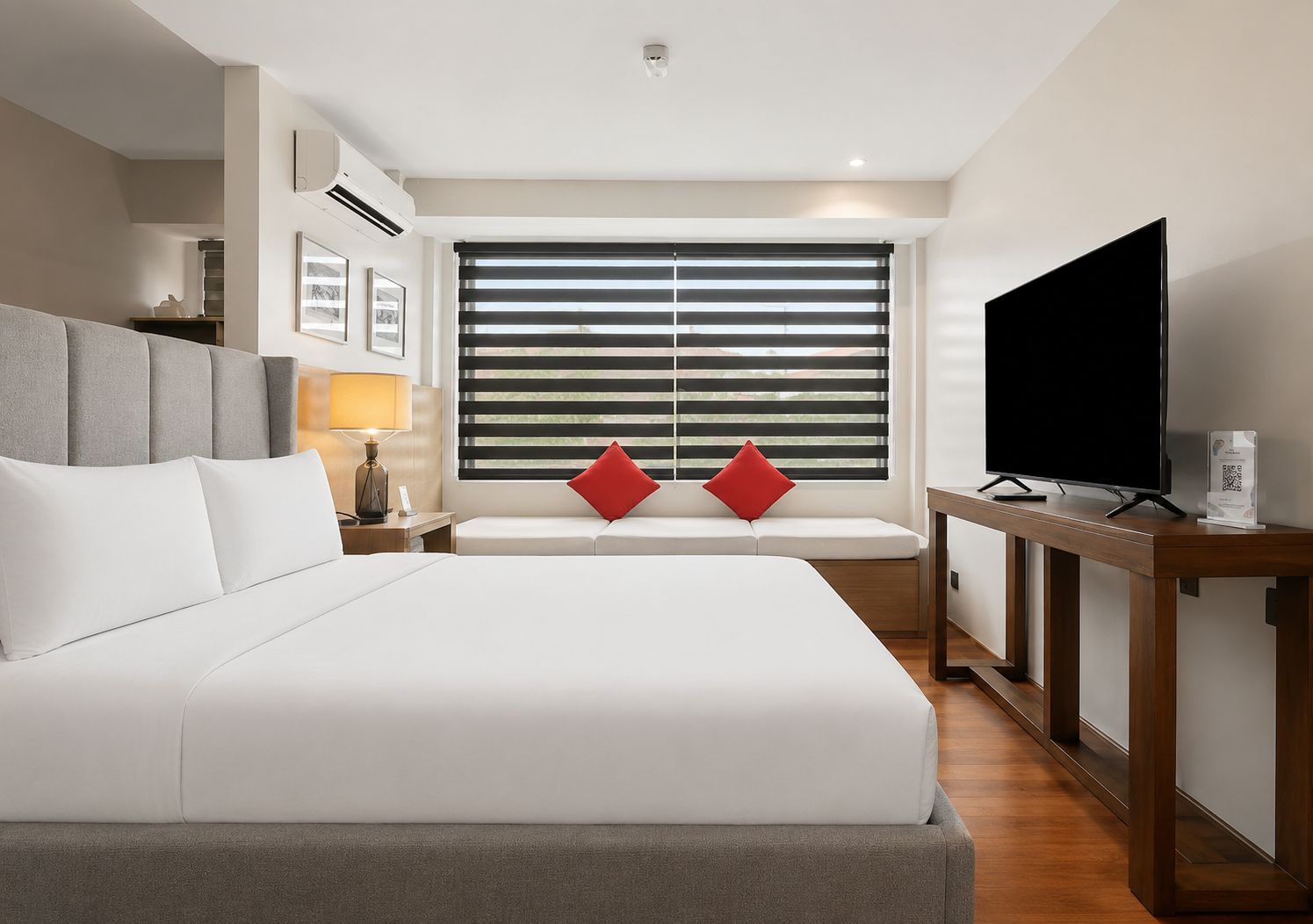 Habitación de hotel con una cama grande, televisión, mesita de noche y ventana con persianas.