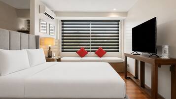 Habitación de hotel con una cama grande, televisión, mesita de noche y ventana con persianas.