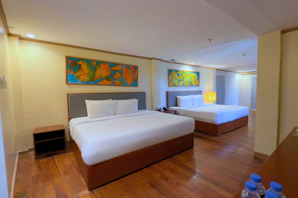 A hotel room with two beds, wooden flooring, and colorful artwork on the walls.