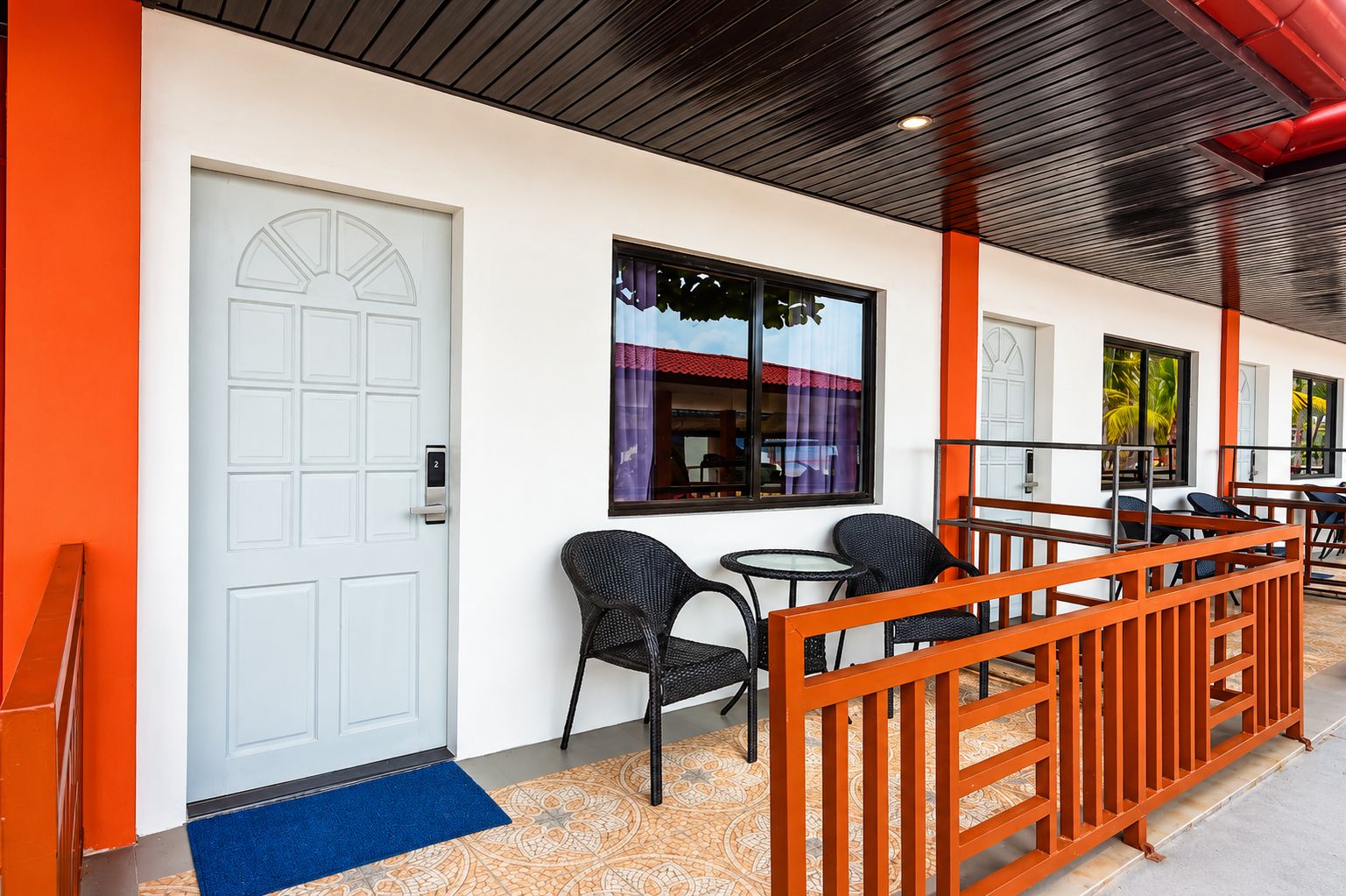 A hotel room with a white door, a small table, two chairs, and a blue doormat.