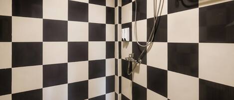 A bathroom with black and white checkered tiles, a shower with a handheld showerhead, and a wall-mounted control panel.