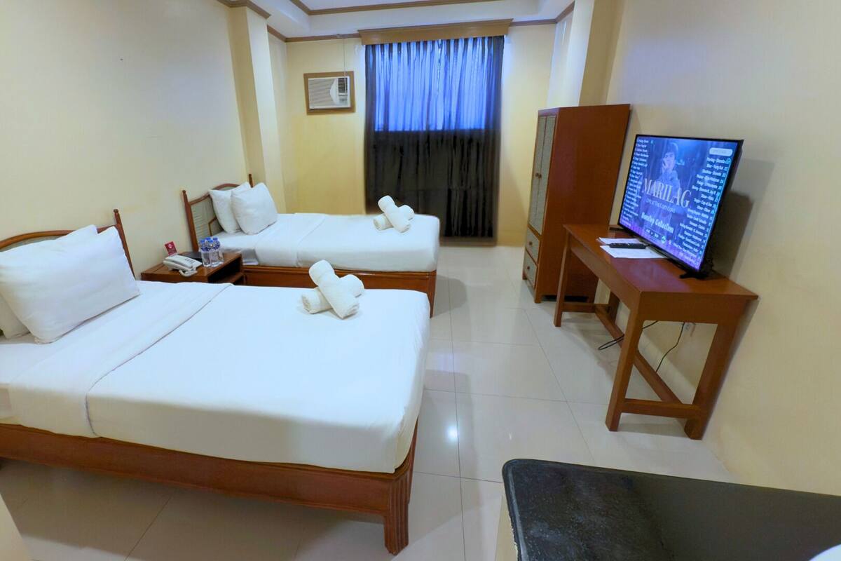 A hotel room with two beds, a desk with a computer, and a TV.
