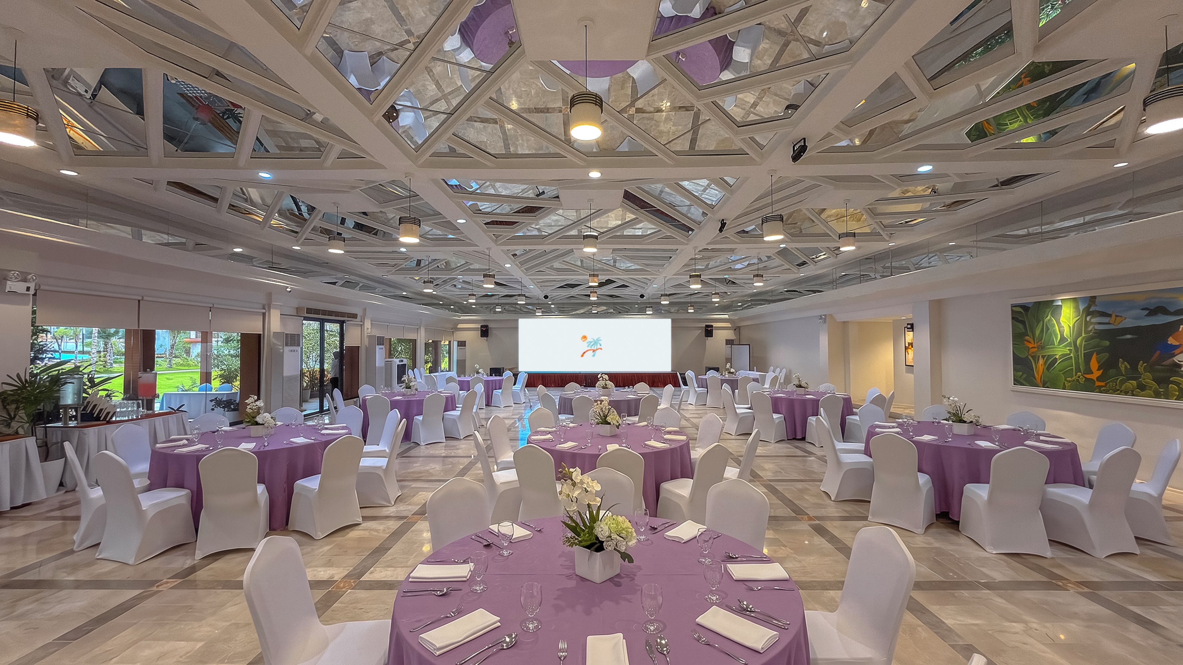 A conference room with round tables, white chairs, and a large screen at the front.