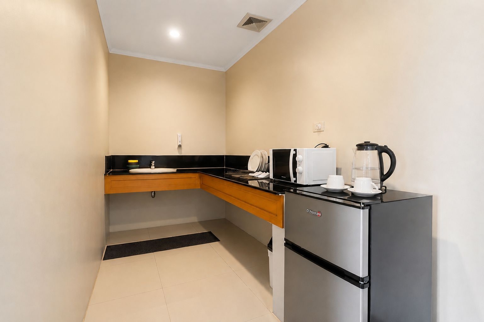 A compact kitchenette with a refrigerator, microwave, kettle, and a small sink.