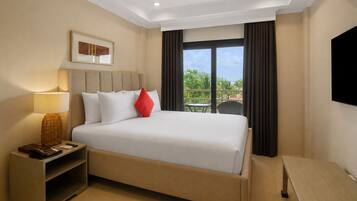 A hotel room with a bed, bedside table, lamp, and a view of greenery through the window.