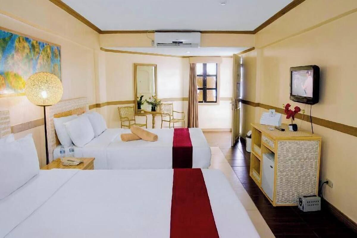 A hotel room with two beds, a desk, a television, and a window.