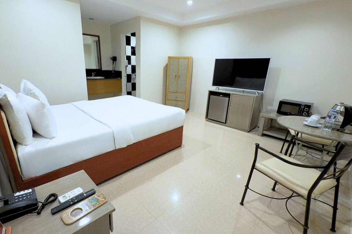 A hotel room with a bed, a desk with a chair, a TV, a microwave, and a small kitchenette.