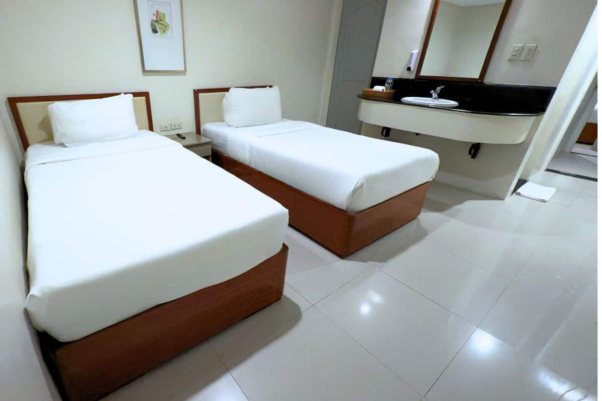 Habitación de hotel con dos camas, baño con lavamanos y espejo.