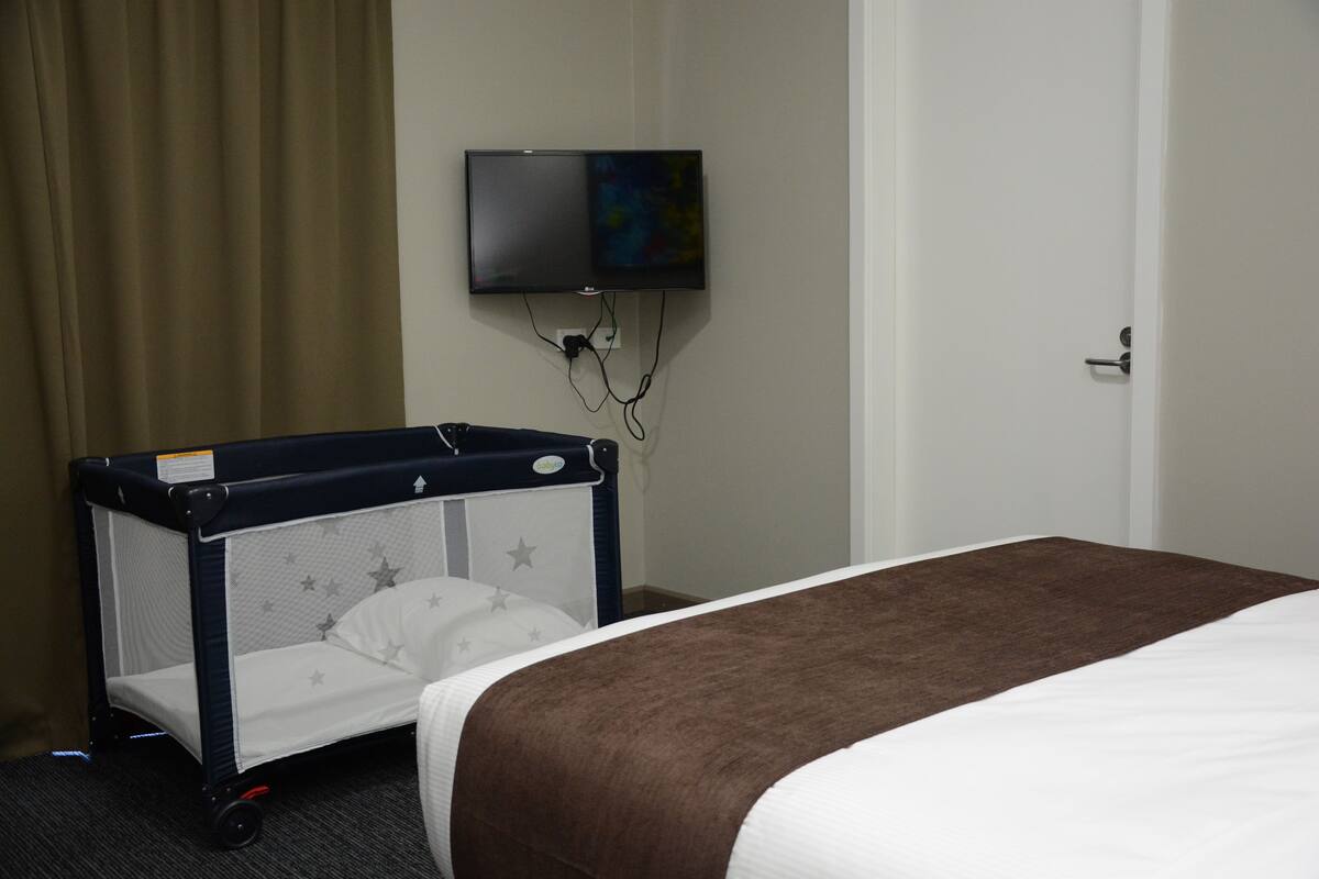 Habitación de hotel con cama, cuna, televisor montado en la pared y una puerta.