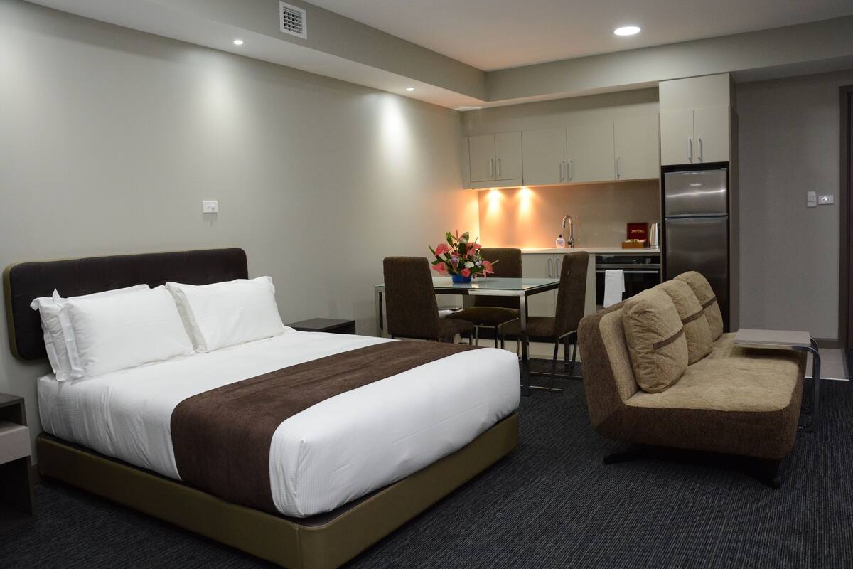 Una habitación de hotel con cama, sofá, escritorio con silla y kitchenette.