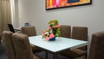 A conference room with a glass table, six brown upholstered chairs, a laptop on a desk, and a colorful abstract painting on the wall.
