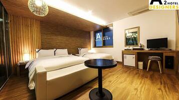 A hotel room with a bed, a desk, a chair, a small table, a television, and a wall-mounted artwork.