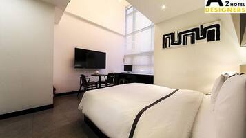 A hotel room with a bed, a desk, a chair, a flat-screen TV, and a window with blinds.