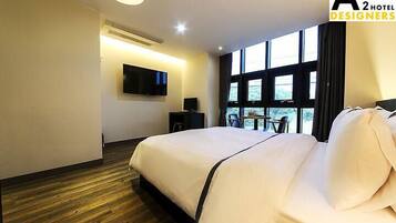 A hotel room with a large bed, a flat-screen TV mounted on the wall, and a window providing a view of the outdoors.
