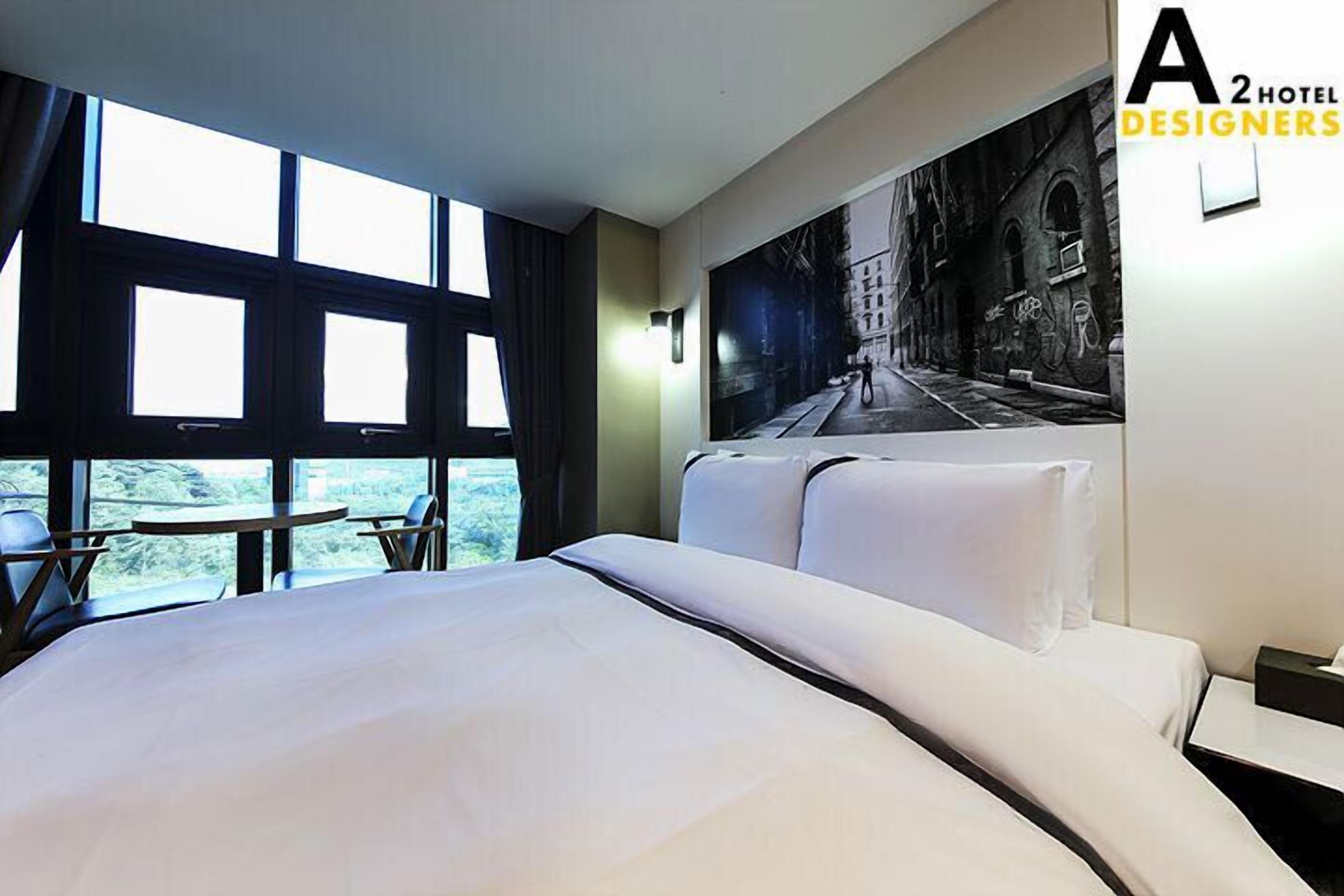 A hotel room with a large bed, a small table, and a view of the outdoors through large windows.