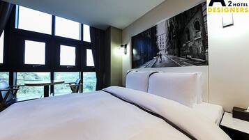 A hotel room with a large bed, a small table, and a view of the outdoors through large windows.