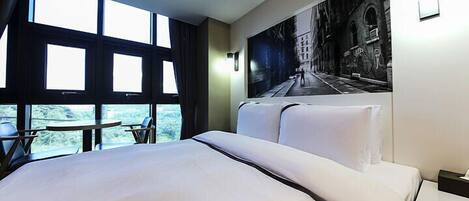 Habitación de hotel con una cama grande, una mesita pequeña y vistas al exterior a través de amplios ventanales.