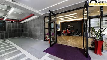 A modern hotel lobby with a glass door entrance, a red scooter, and a purple carpet.