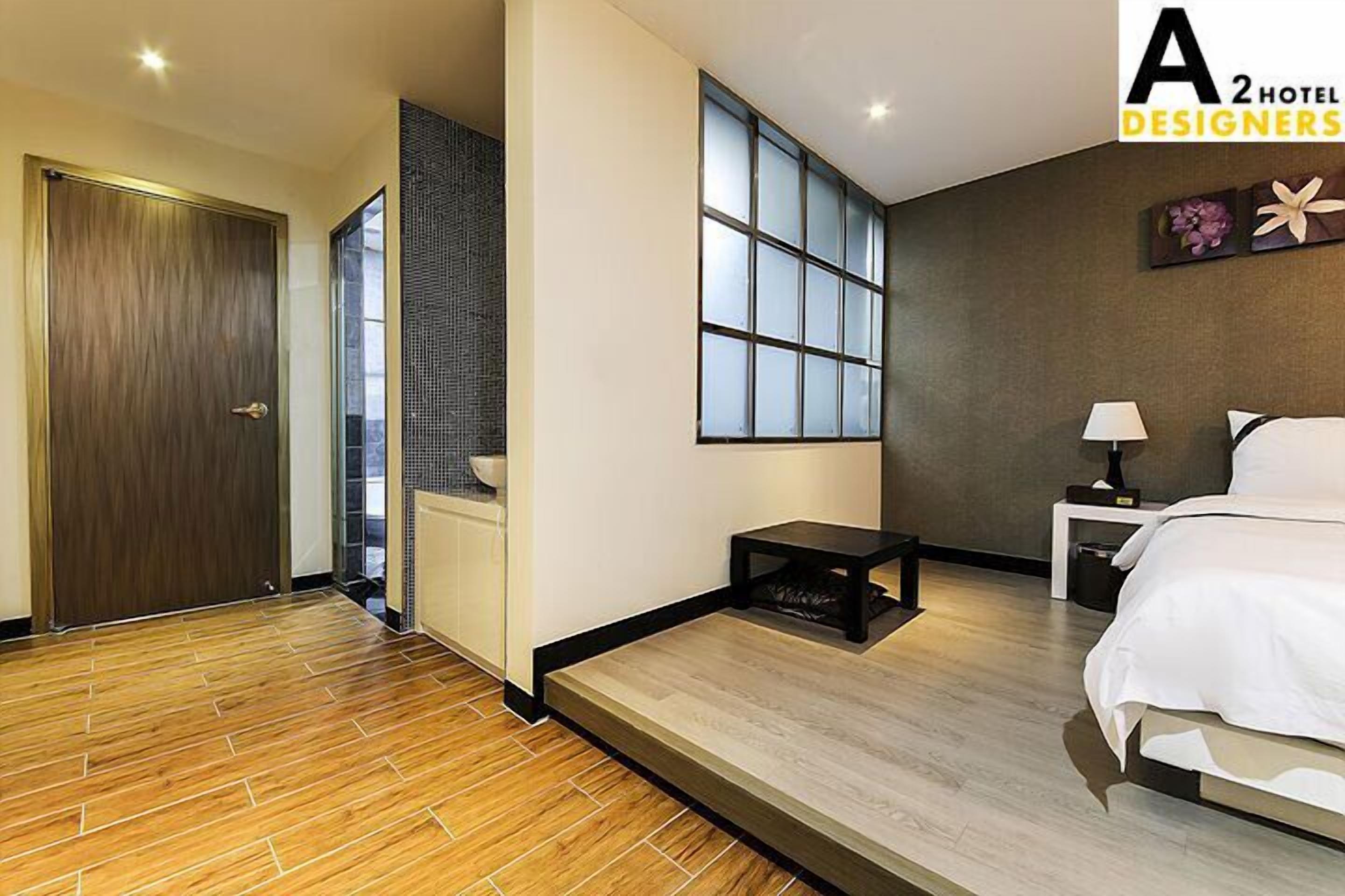 A modern hotel room with a large bed, a small bedside table, a nightstand, a window, and a door.