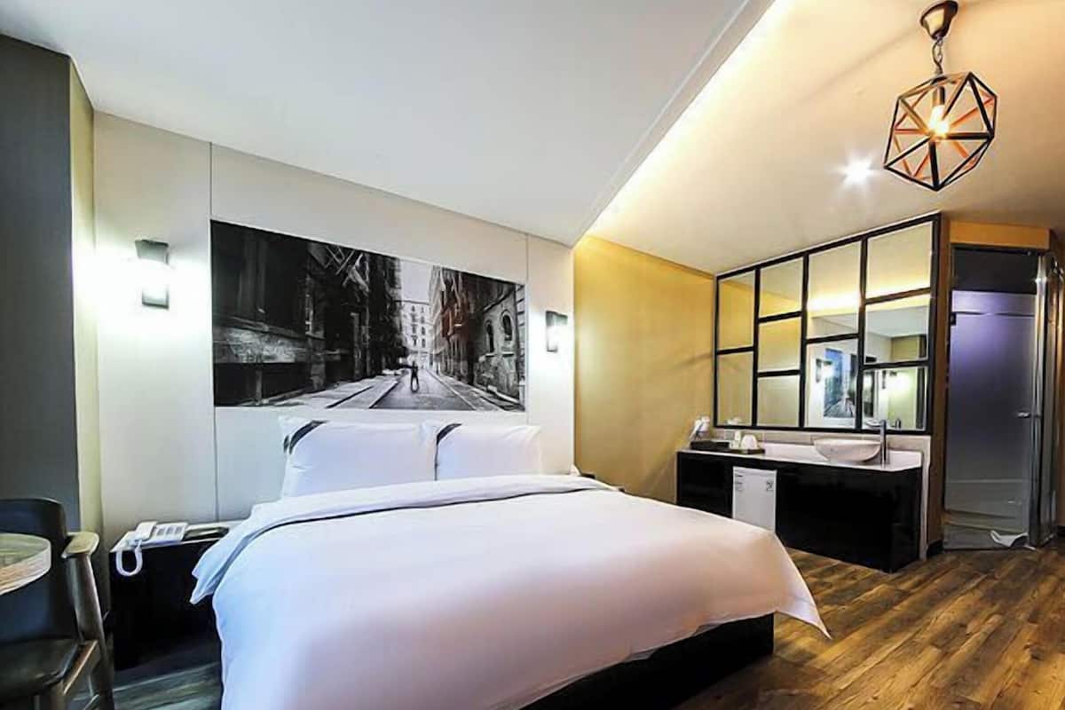 Una habitación de hotel moderna con una cama grande, un escritorio, una silla, un espejo y vistas a una calle de la ciudad.