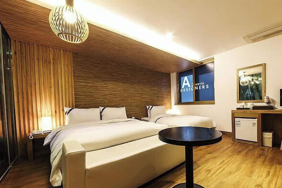 Habitación de hotel con una cama grande, mesitas de noche, un escritorio pequeño, una silla, una mesa redonda y una lámpara colgante.