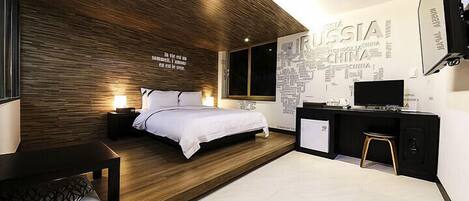 A modern hotel room with a wooden accent wall, a bed, bedside tables, a desk, and a TV.