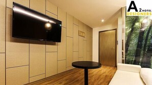 Una habitación de hotel moderna con una televisión de pantalla plana montada en la pared, una mesa redonda negra y un sofá blanco.