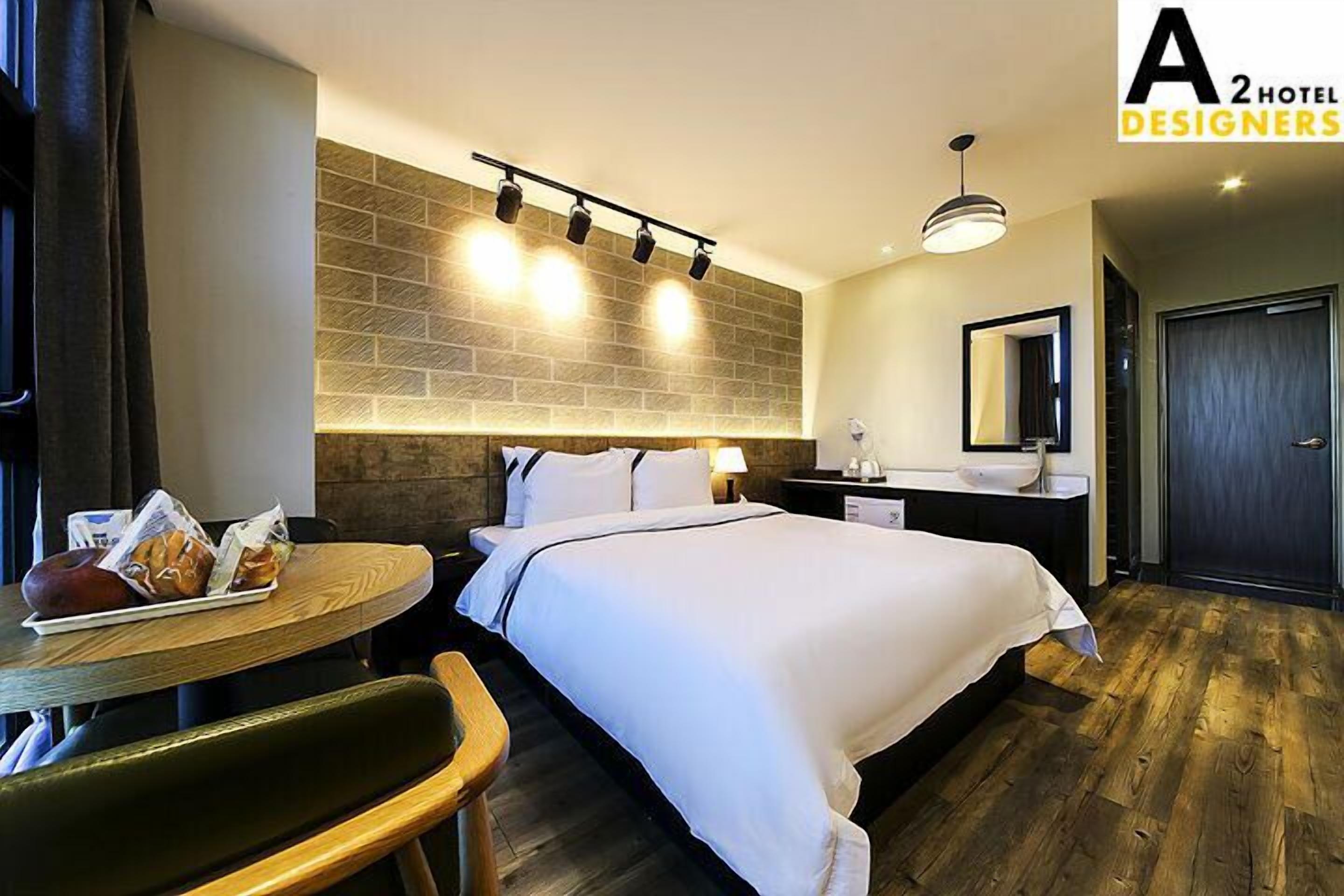 A hotel room with a bed, bedside table, and a small dining table with breakfast items.
