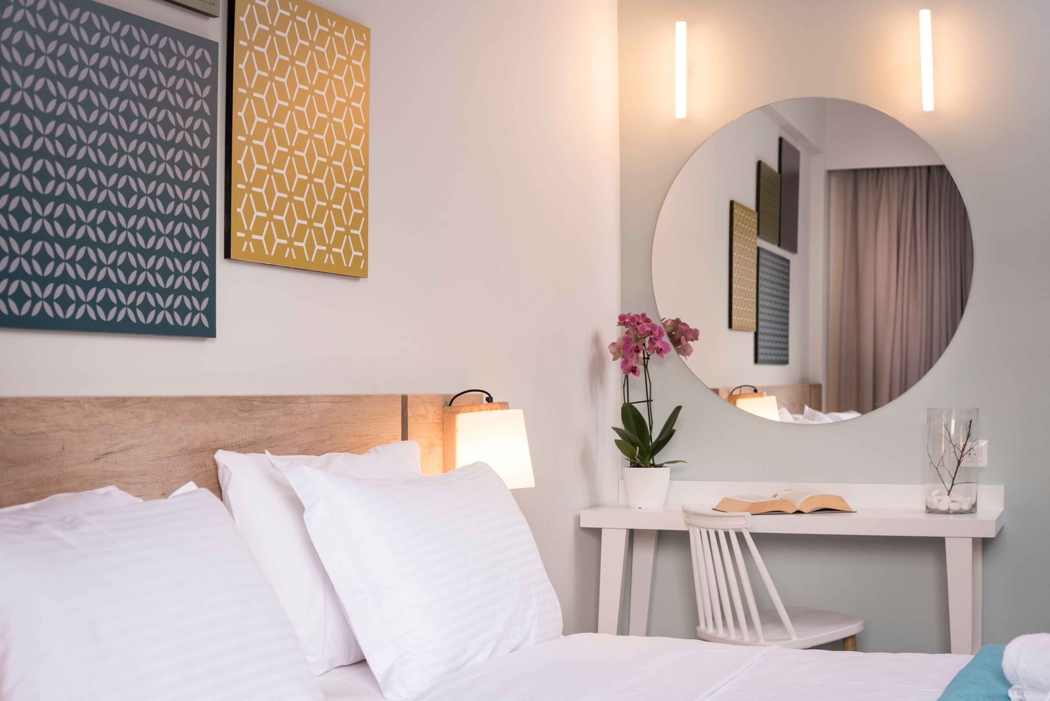 A hotel room with a bed, a desk, a chair, a potted plant, and a mirror.