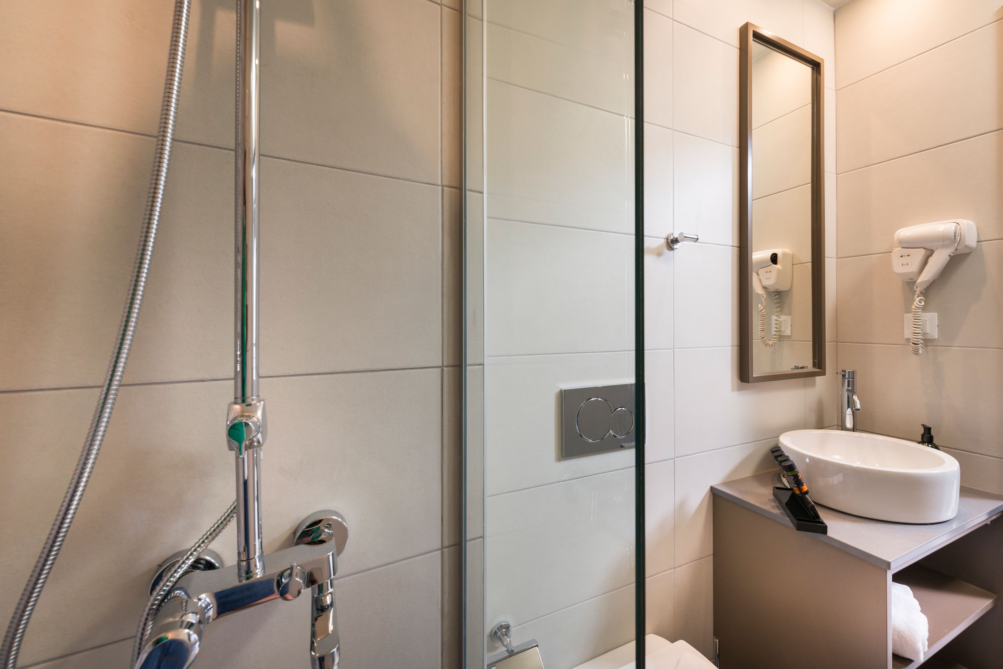 Ein modernes Badezimmer mit Duschkabine aus Glas, einem weißen Waschbecken und einem an der Wand befestigten Föhn.