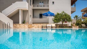 A swimming pool with clear blue water, a stone wall, and a few lounge chairs. - Irini Stalos Apartments (Chania)