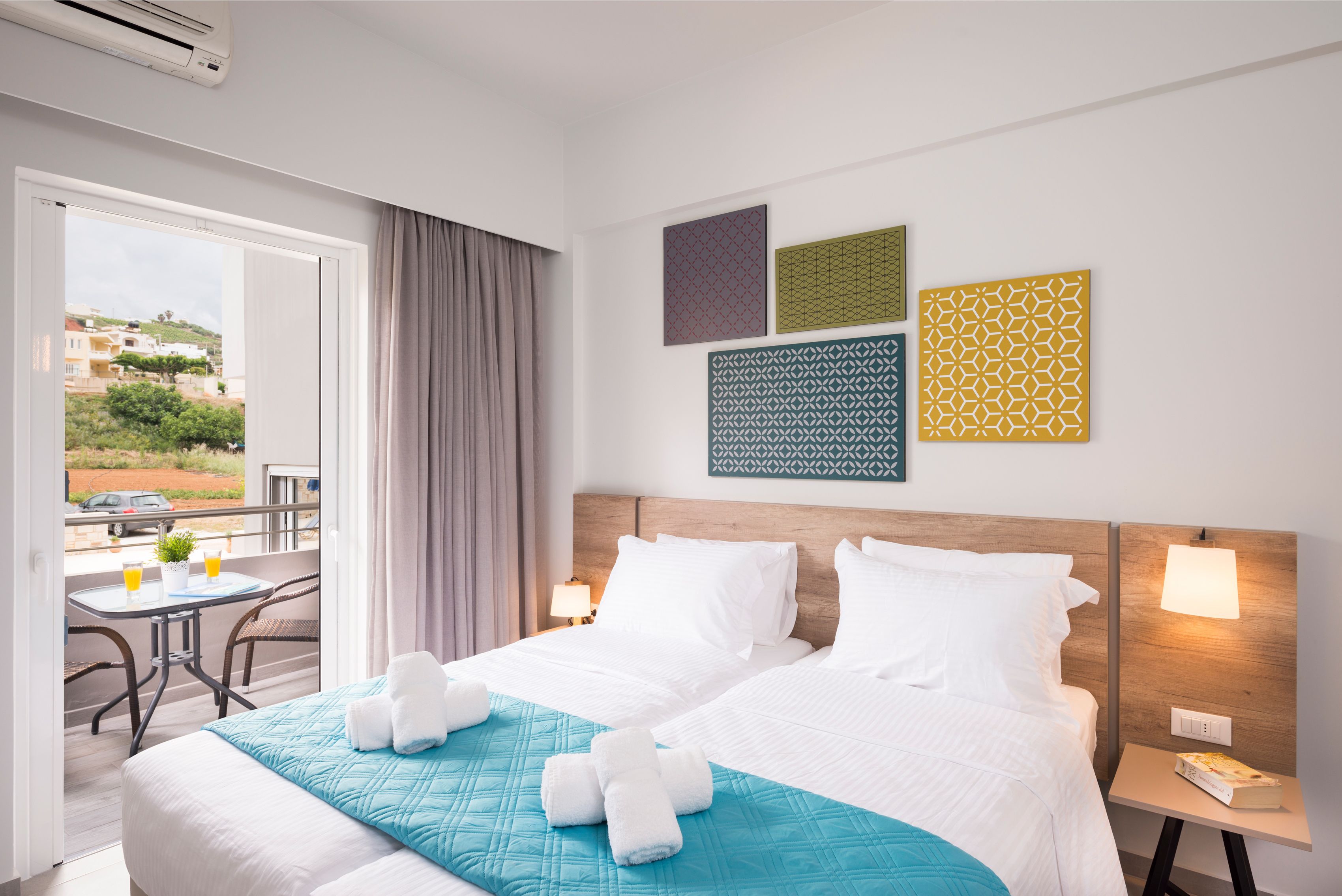 Een hotelkamer met twee bedden, een balkon met een tafel en stoelen, en kunst aan de muur.
