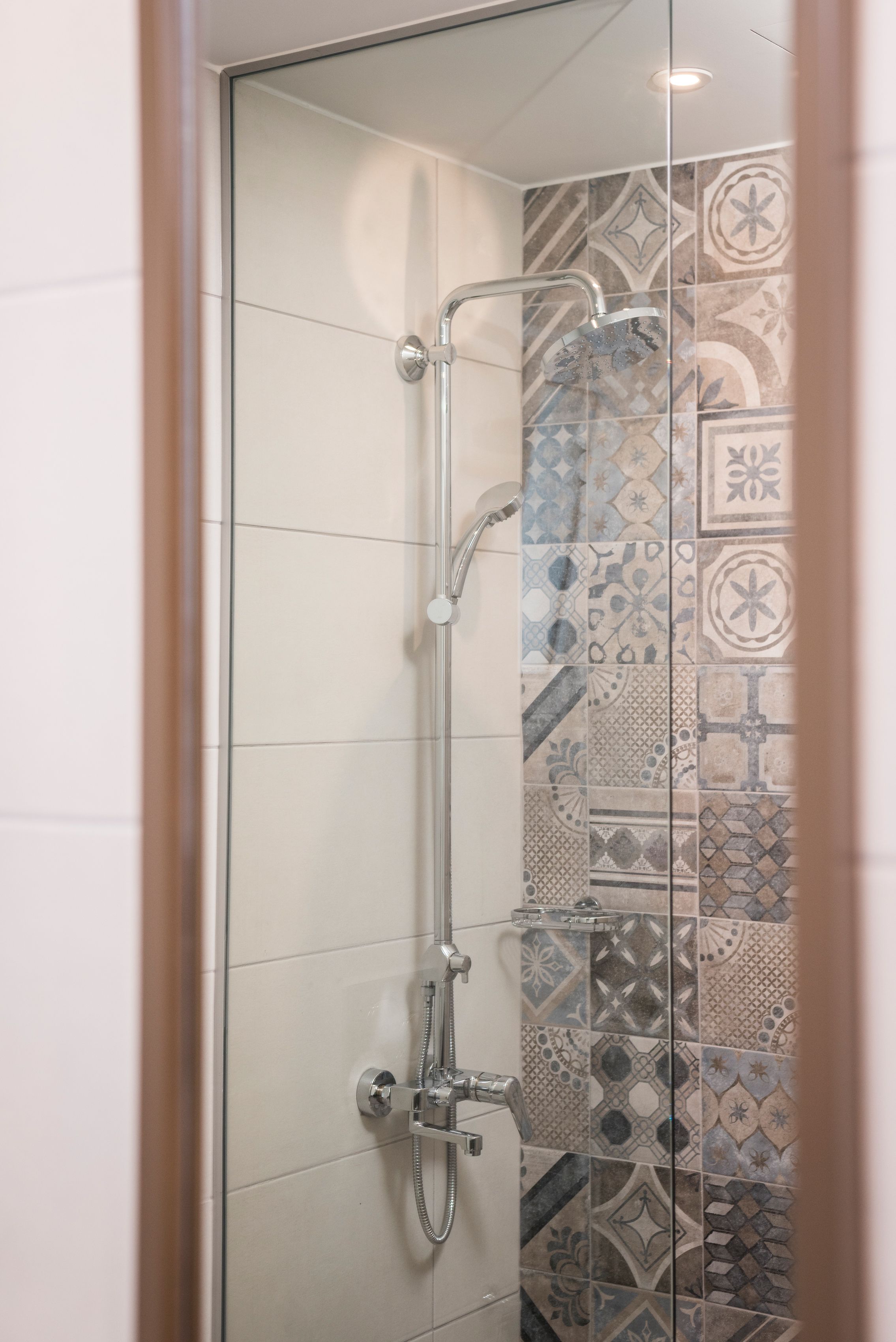 A glass-enclosed shower with a chrome showerhead and handheld shower attachment.