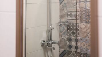 A glass-enclosed shower with a chrome showerhead and handheld shower attachment.