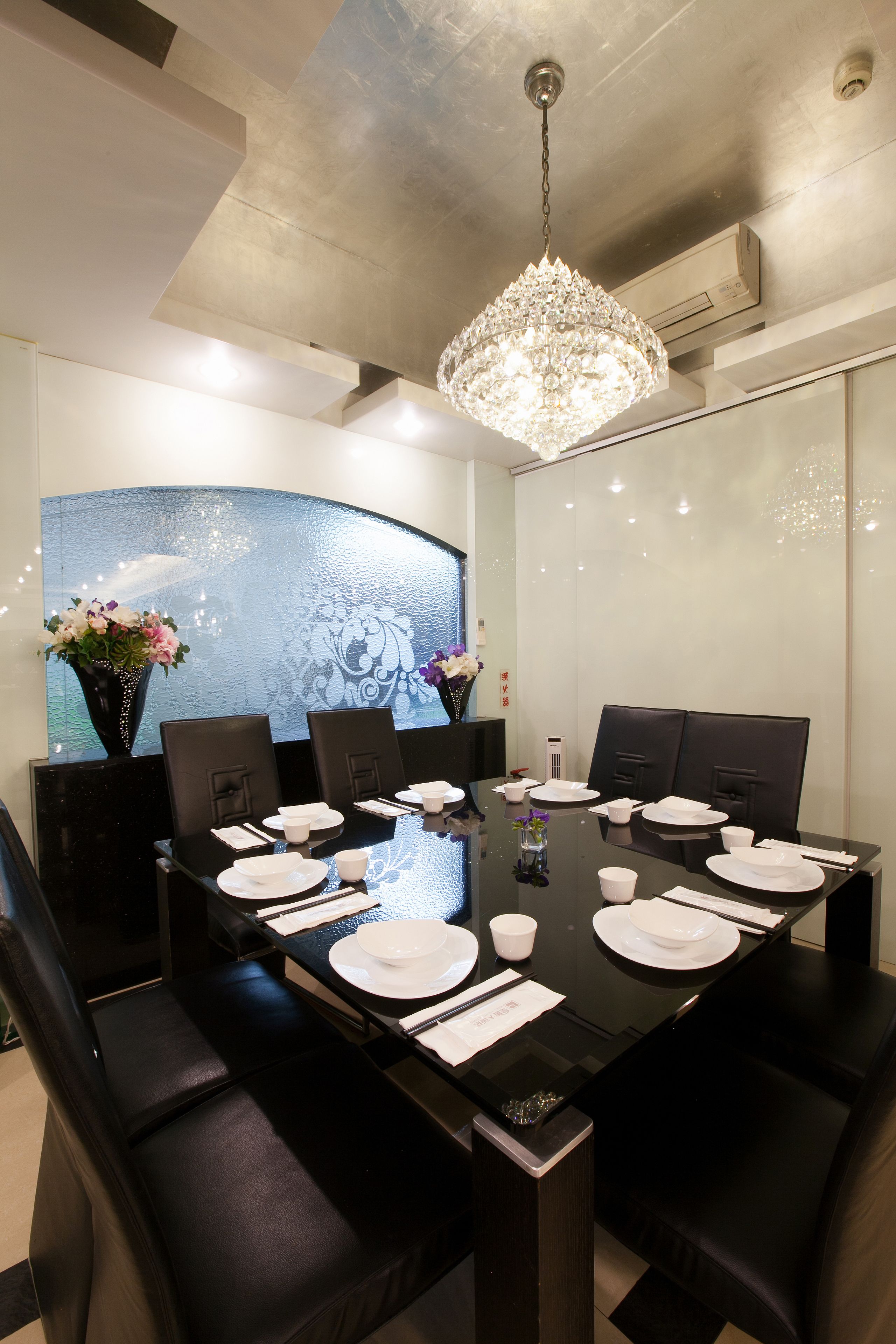 A modern dining area with a black table set for six, surrounded by black chairs.