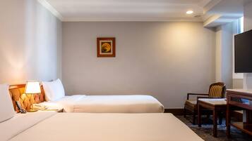 A hotel room with two beds, a desk, a chair, a lamp, and a painting on the wall.