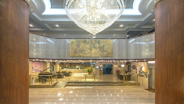 Um hall amplo com um lustre imponente, balcão de recepção e um piano.