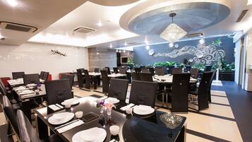 A modern dining area with black and white checkered flooring, black chairs, and tables set with white plates and cutlery.