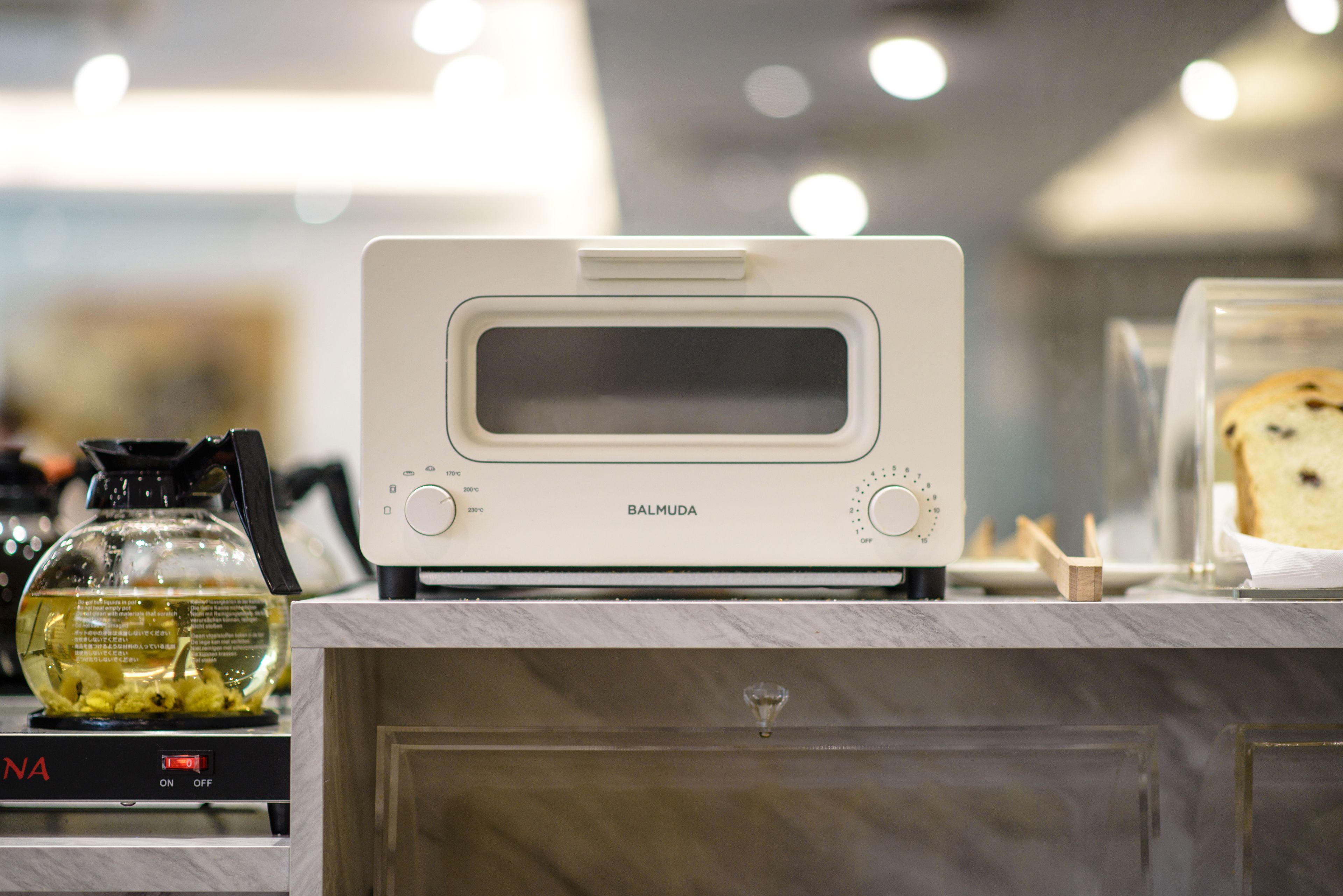 A kitchen with a modern toaster oven, a glass container with a yellow liquid, and a loaf of bread on a counter.