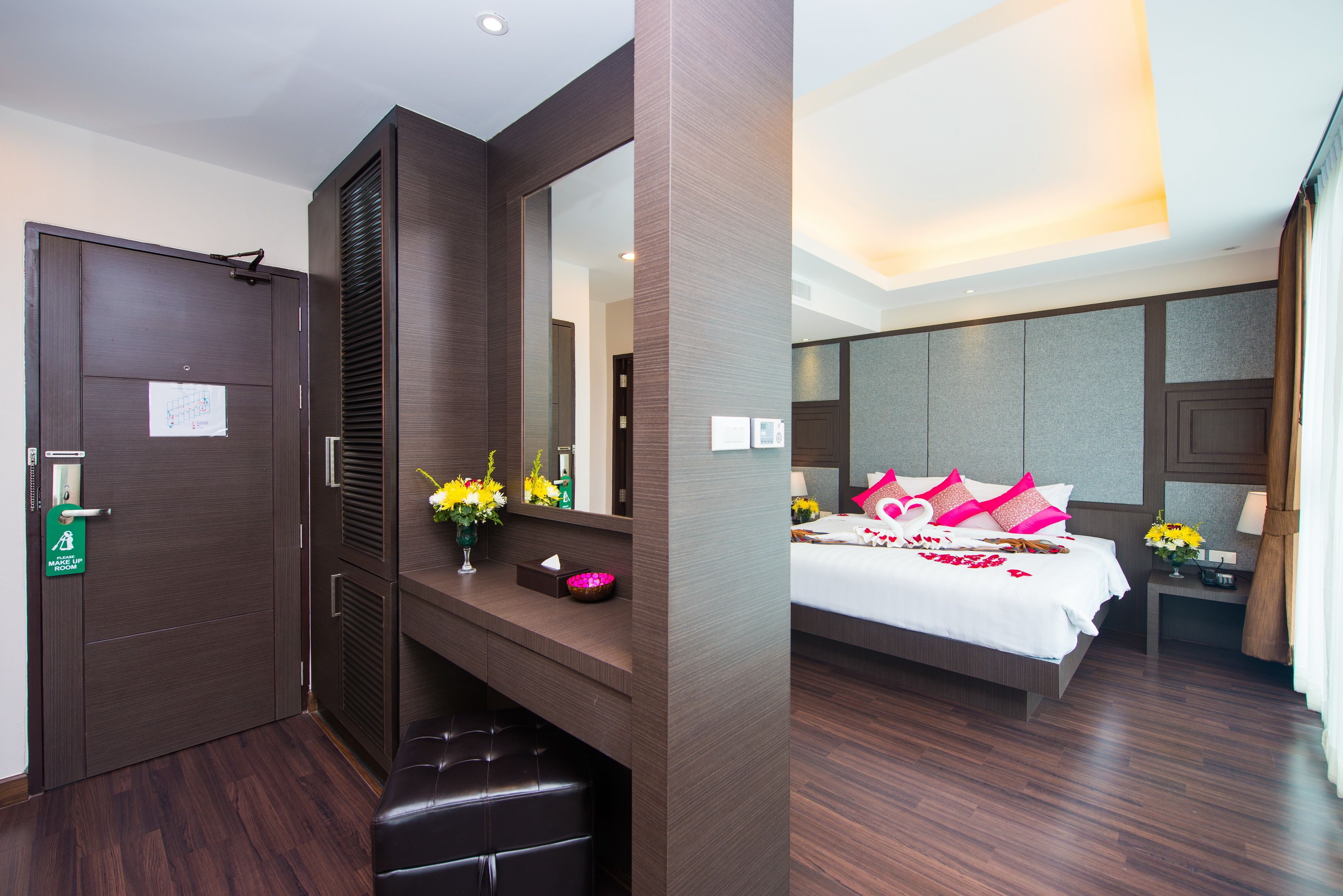 A hotel room with a large bed, a bedside table with a lamp, a mirror, and a door with a green sign.