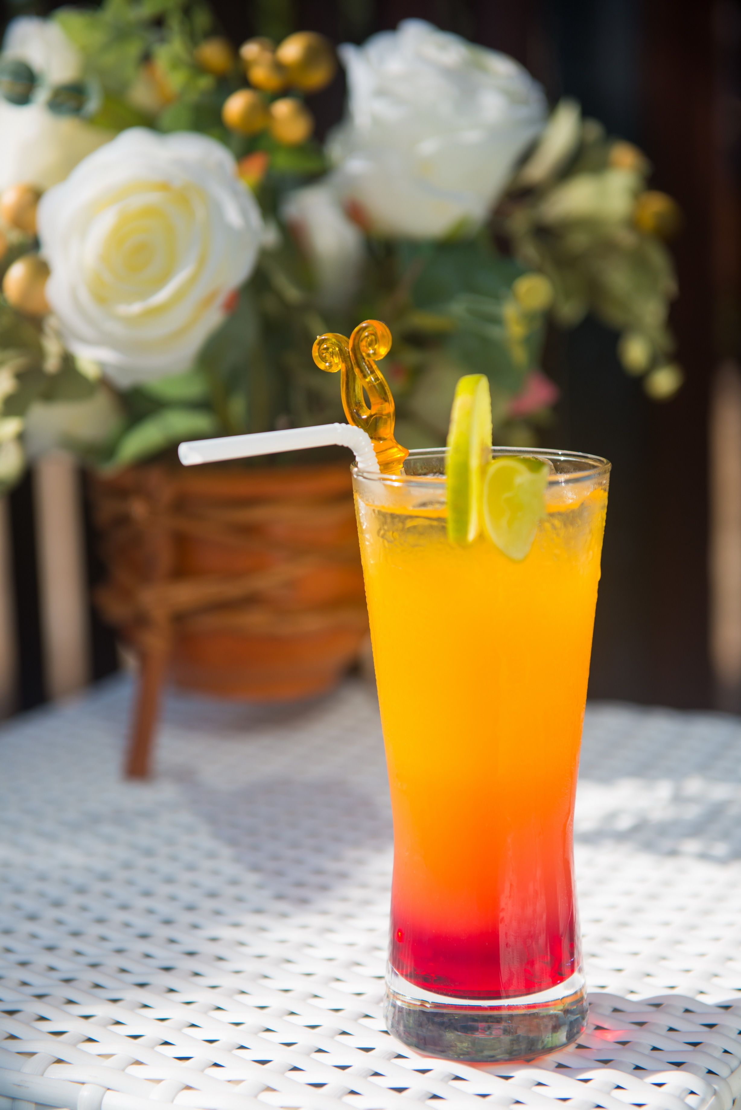 Un grand verre contenant une boisson aux couleurs dégradées, une paille et une tranche de citron vert, posé sur une table blanche ornée d’un motif en treillis métallique.