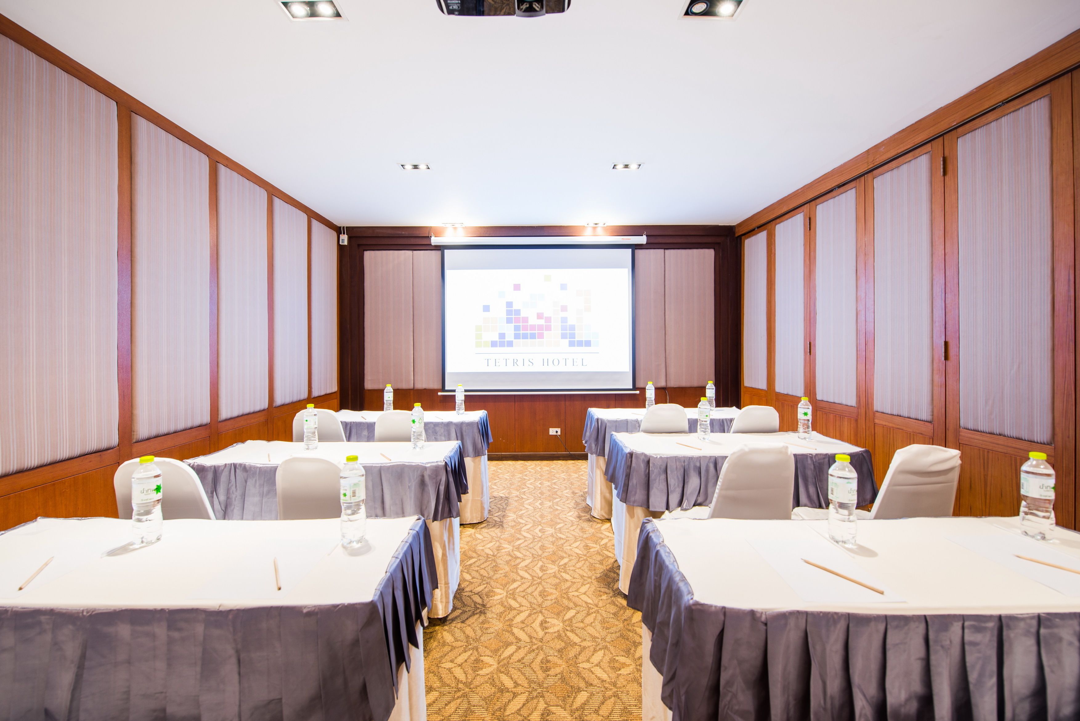 A conference room with tables, chairs, and a projector screen displaying 'TETRIS HOTEL'.