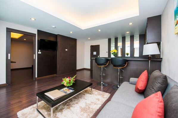 A modern living room with a sofa, coffee table, and two bar stools. - Tetris Hotel (Krabi)