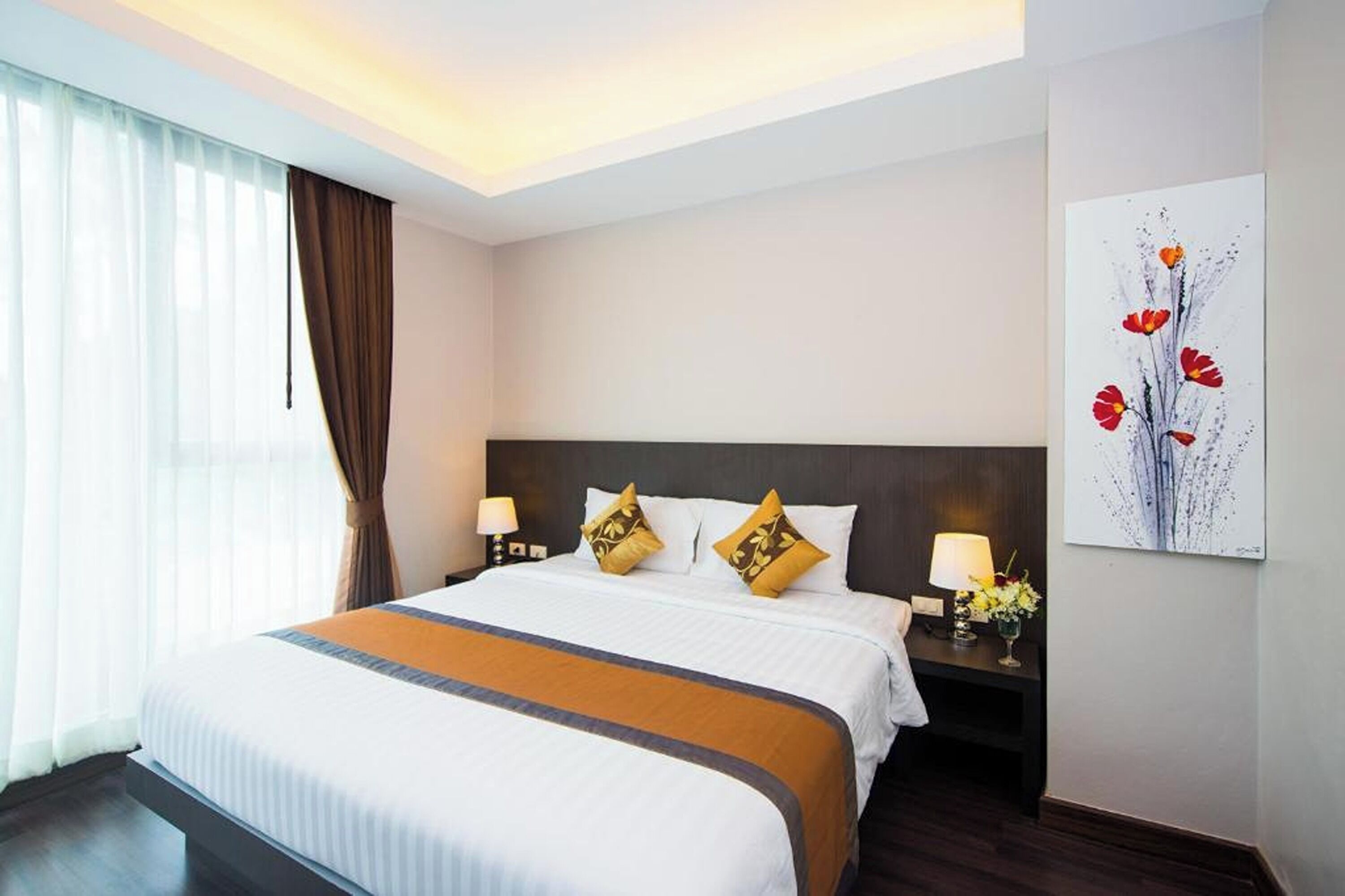 A hotel room with a large bed, two bedside tables with lamps, a window with curtains, and a wall art piece.