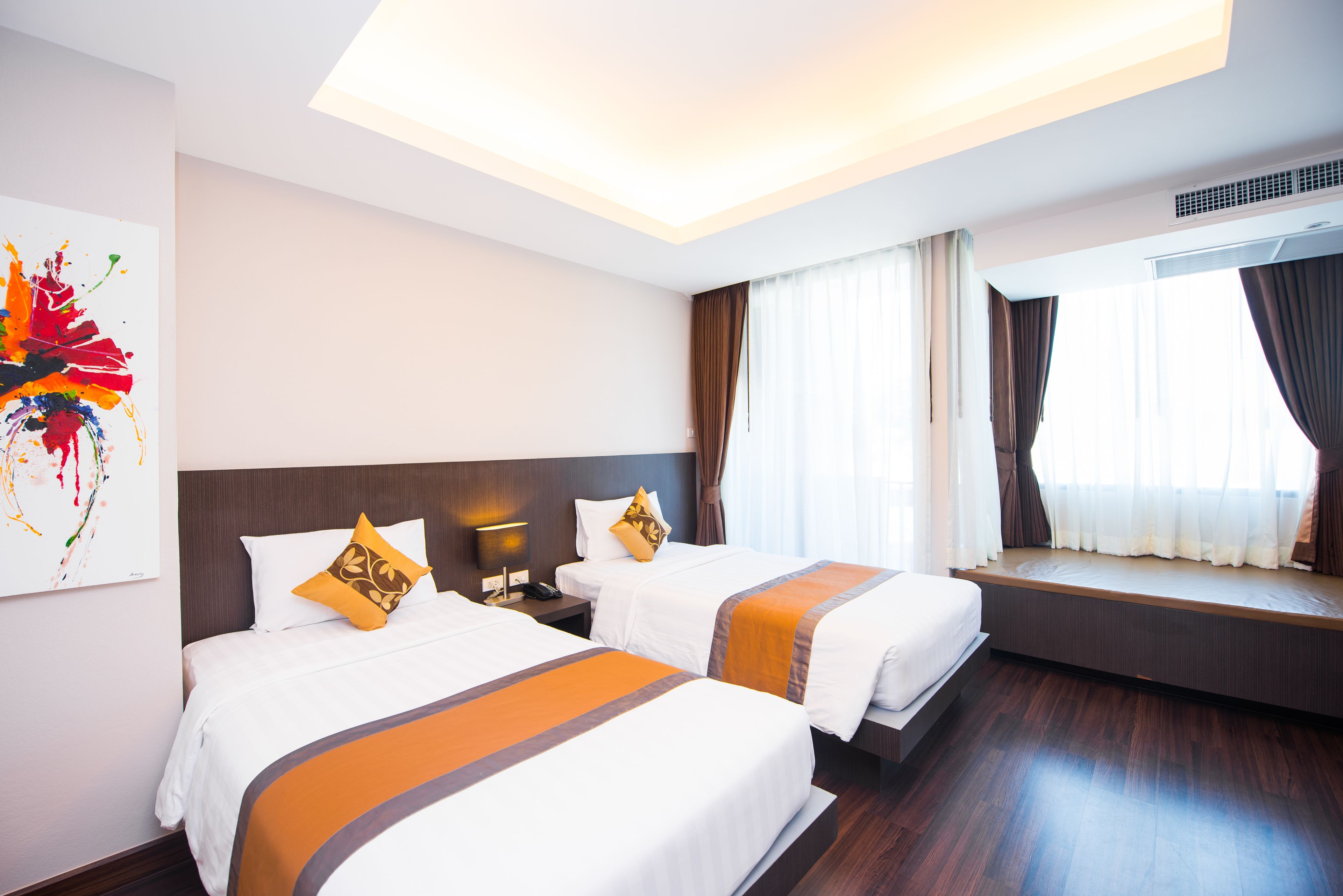 Quarto de hotel com duas camas, uma janela grande com cortinas, uma luminária no teto e um quadro na parede.